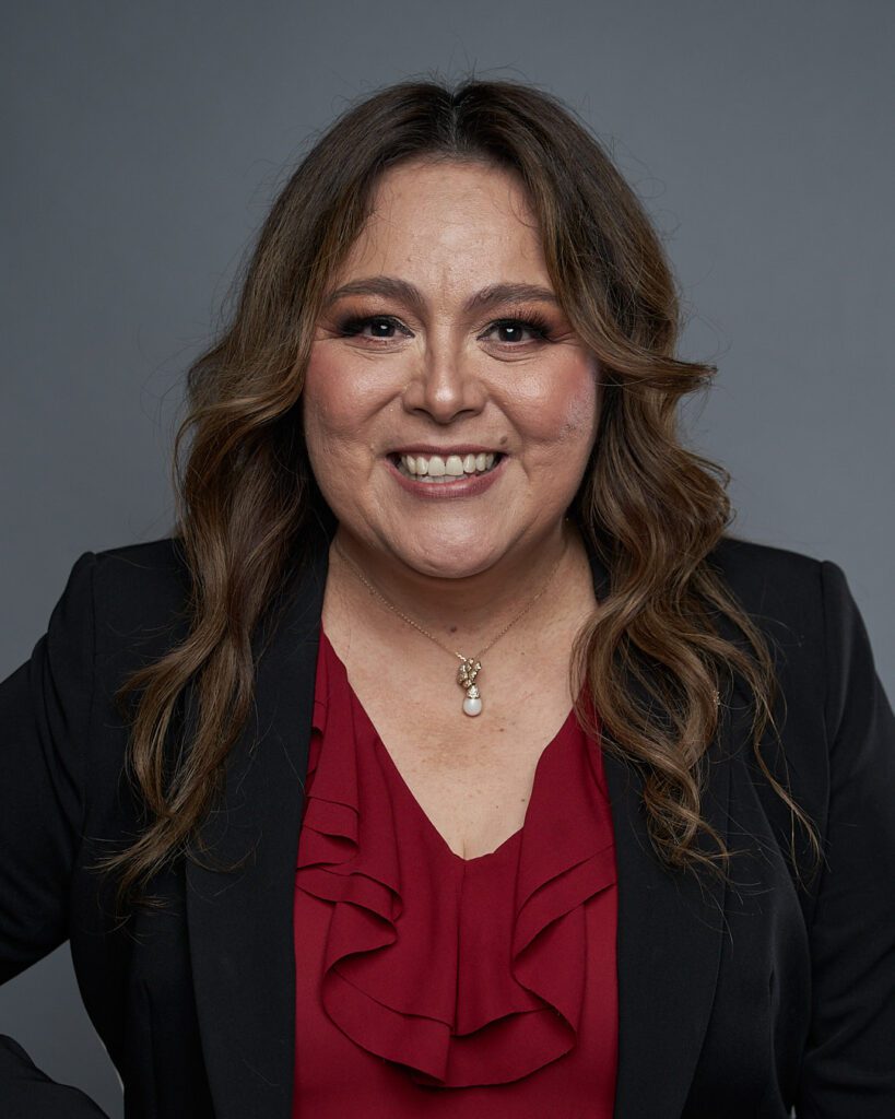 Ejemplo de Foto Perfil LinkedIn para no Fotogénicos de Mujer de cabello castaño ondulado mirando con la cara sonriente mirando a la cámara con la cara hacia afuera en primer plano mostrando cuello delgado sin papada.